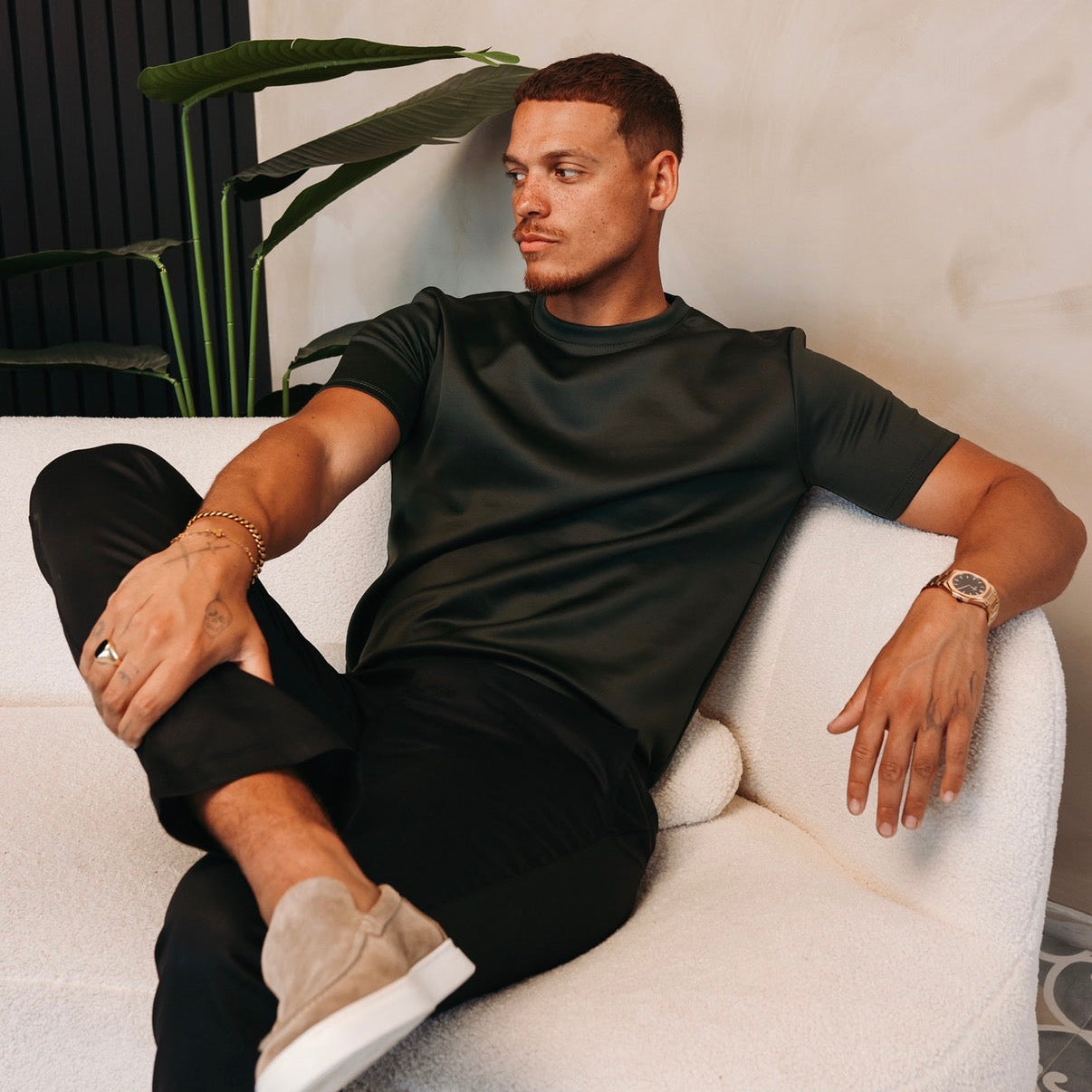 Model zit ontspannen in een witte stoel in het Gloss Essential Shirt in midnight olive