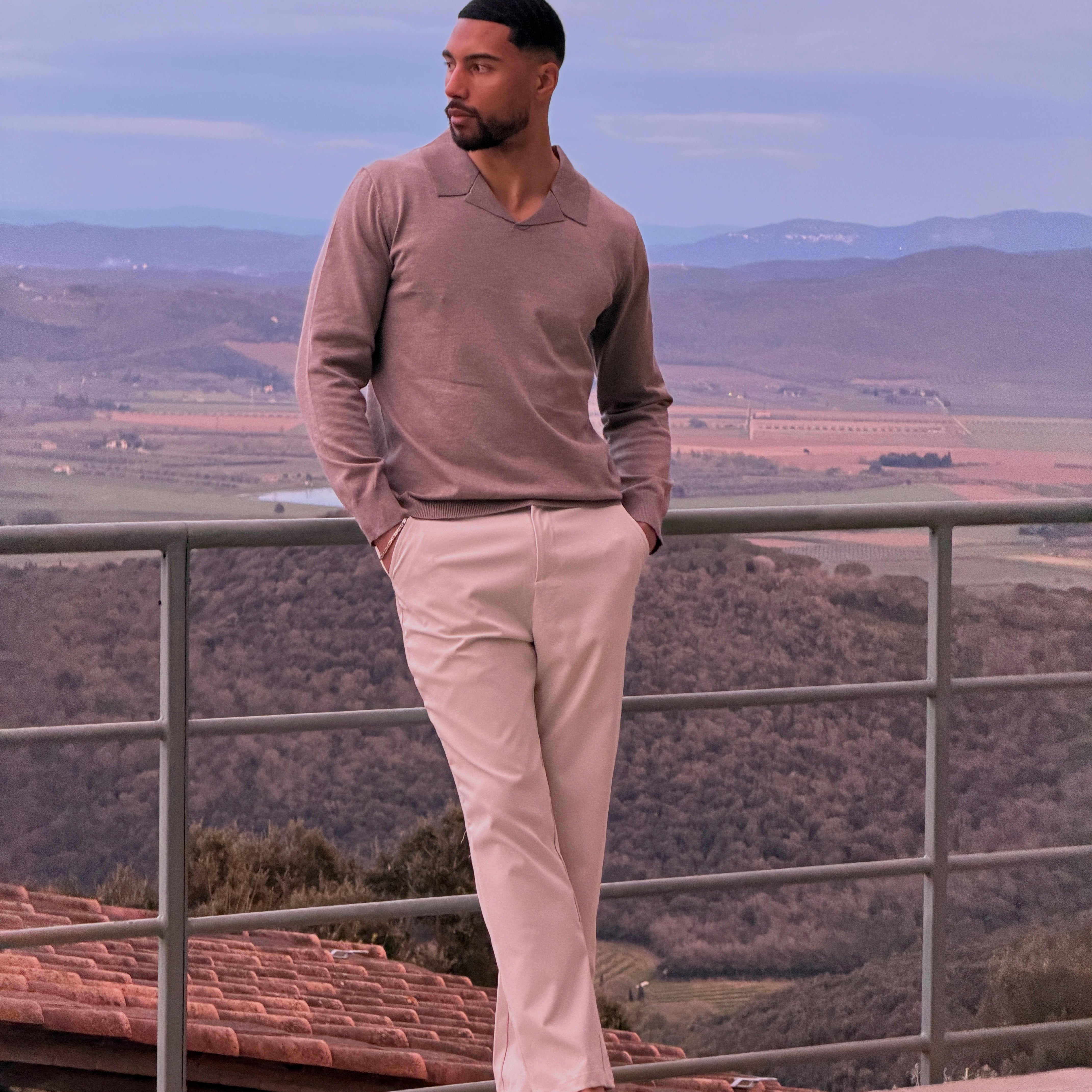 Model in de Renzo Polo in beige op een terras met uitzicht bij zonsondergang