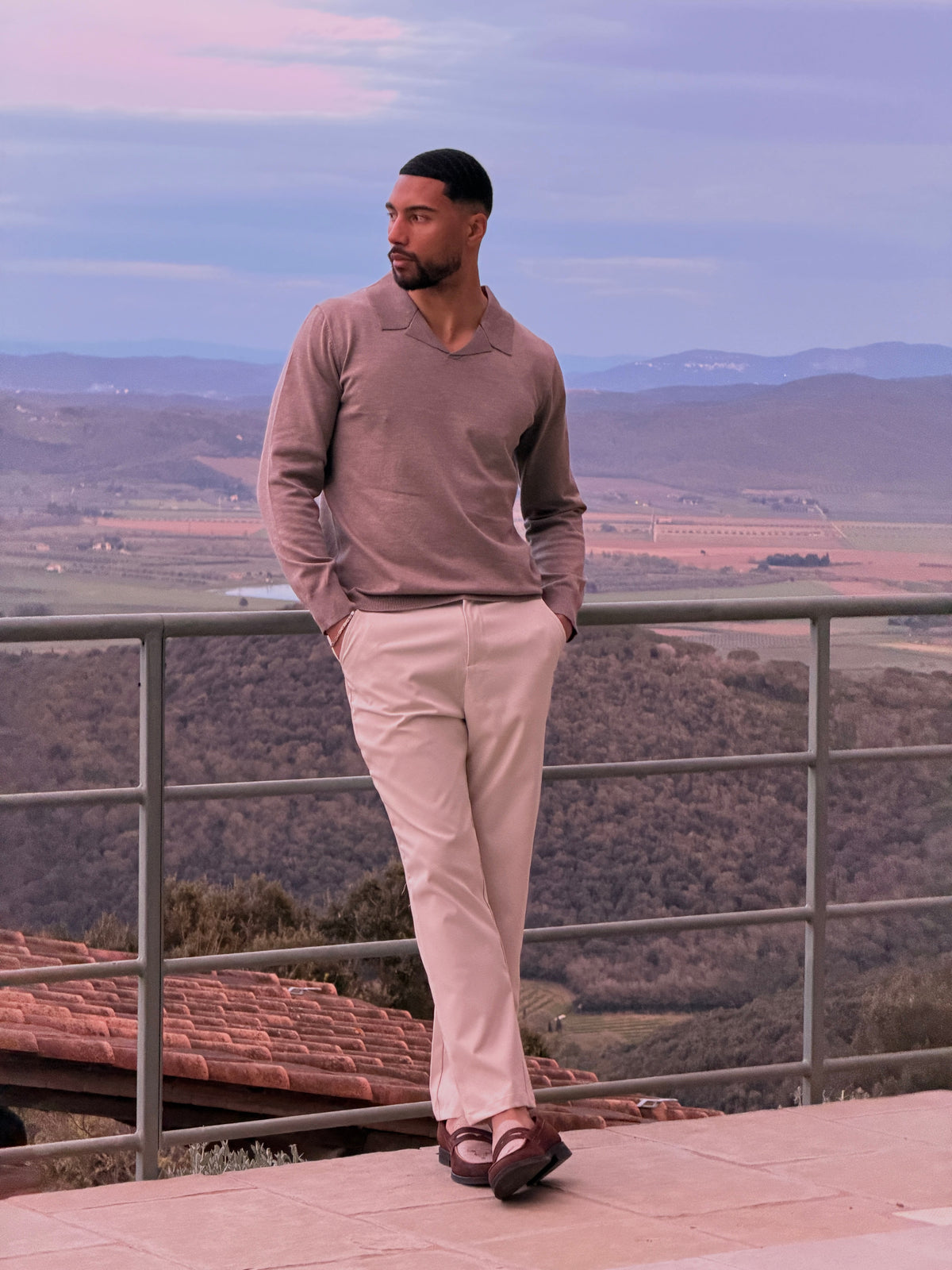 Model in de Renzo Polo in beige op een terras met uitzicht bij zonsondergang