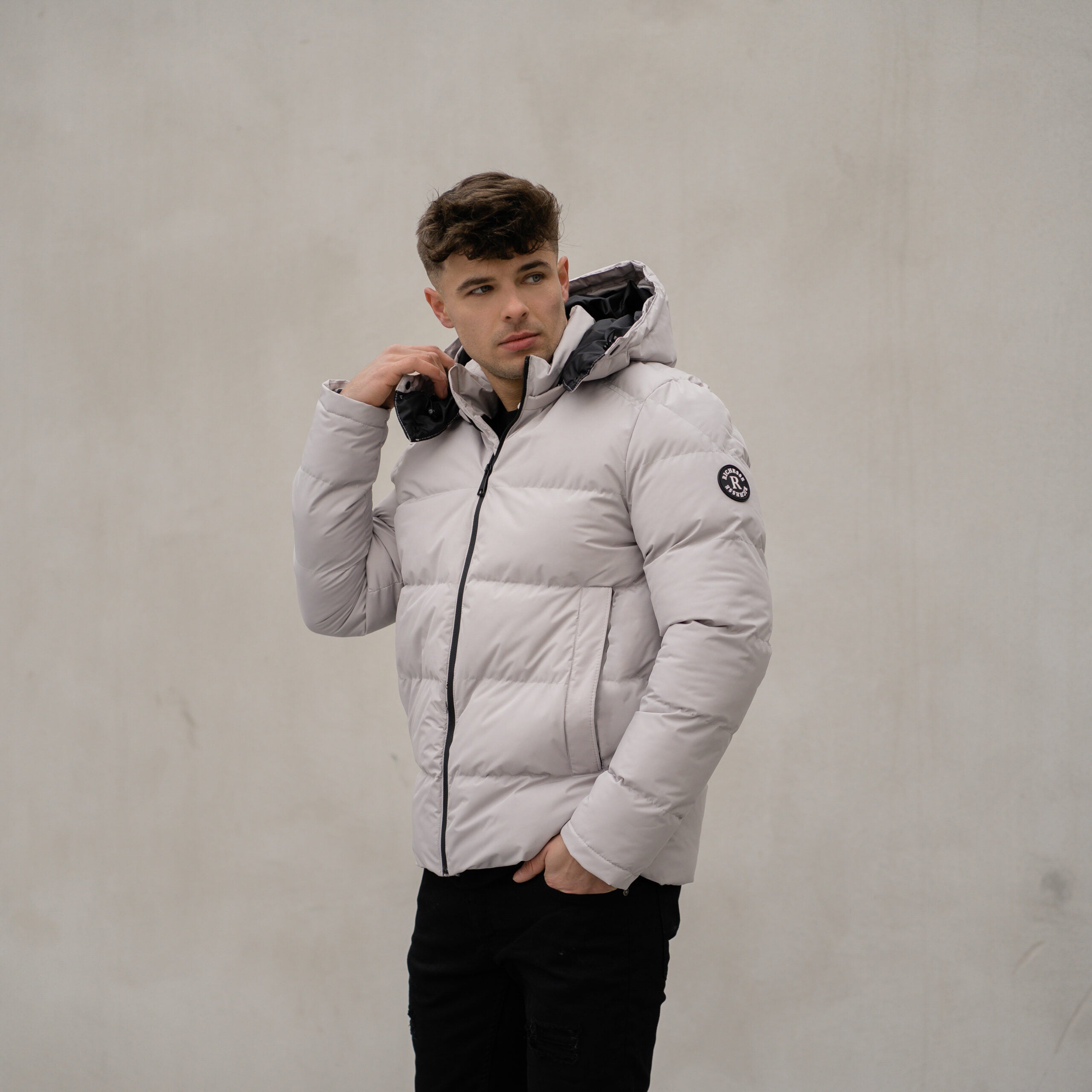 Model in de lichte Devon Puffer Jas met capuchon, tegen een betonnen muur